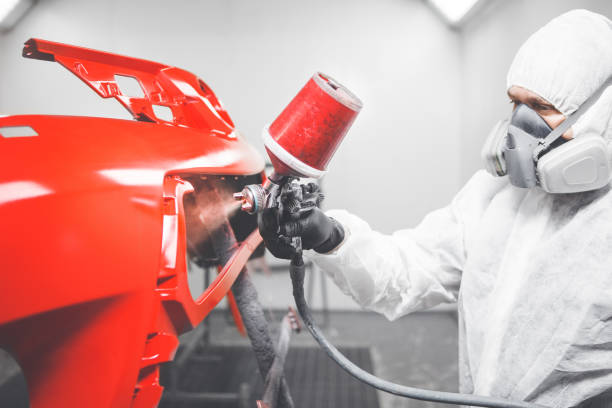 Professional male car painter is painting in garage by airbrush. Man works with spray gun. Painting the car in white. Body repair cars.